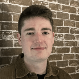 A student poses for a photo in front of a brick wall